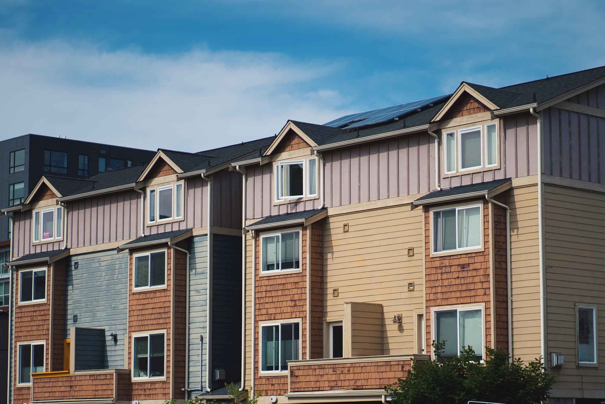Row of three-story townhomes with dark shingle roofs, stepped gables, gutters and downspouts