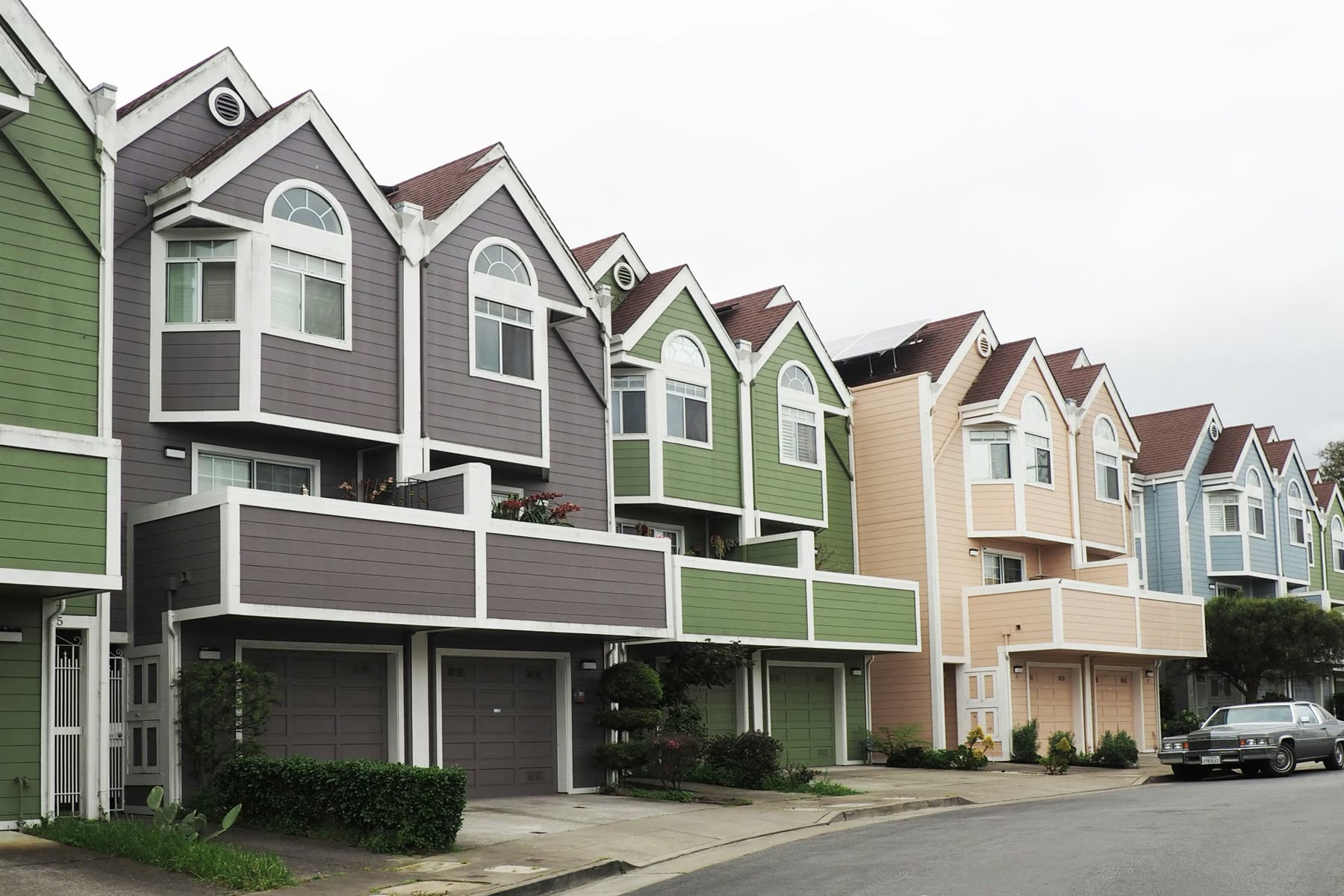 Row of townhomes with garages, short driveways, balconies and front plantings along a curved street