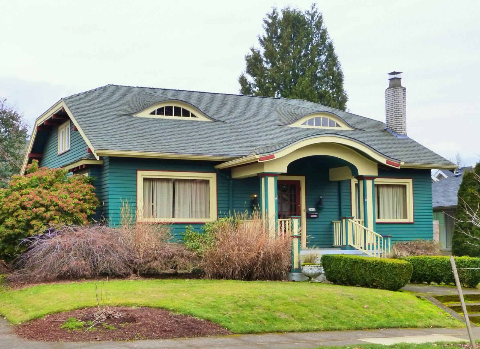 Portland craftsman bungalow with a gray shingle roof and eyebrow dormers, a tall conifer behind it under an overcast winter sky